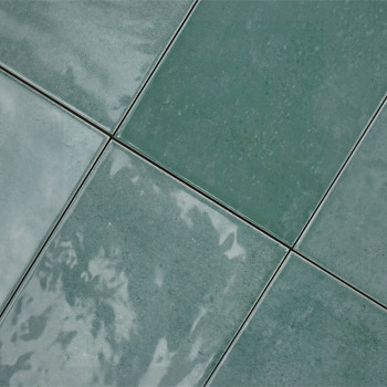 Les carreaux de céramique verte sont disposés selon un motif en grille, réfléchissant la lumière, avec de subtiles variations de