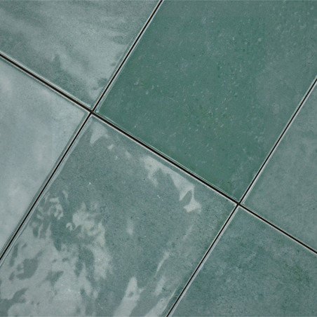 Les carreaux de céramique verte sont disposés selon un motif en grille, réfléchissant la lumière, avec de subtiles variations de