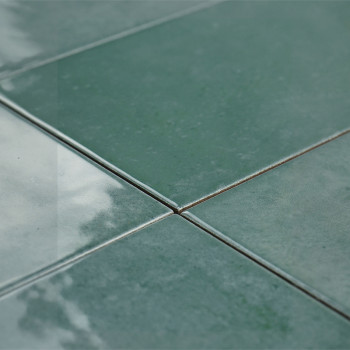 Quatre carreaux verts brillants se rejoignent au centre, réfléchissant la lumière, créant une surface lisse et polie dans un déc