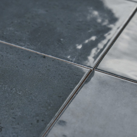 Dunkle, glänzende Keramikfliesen reflektieren das Licht und zeigen eine leicht strukturierte Oberfläche mit subtilen Farbvariati