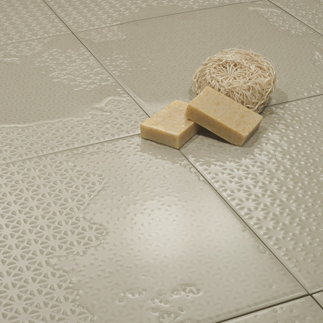 Azulejos de color beige brillante con intrincados patrones en relieve están colocados uno contra el otro, sosteniendo una esponj
