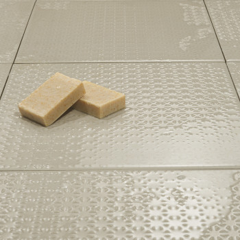 Tegels met een neutrale textuur liggen plat en reflecteren het licht subtiel. Twee rechthoekige zepen rusten bovenop, wat voor c