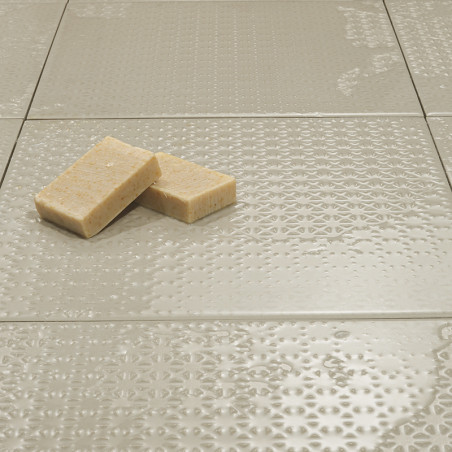 Tegels met een neutrale textuur liggen plat en reflecteren het licht subtiel. Twee rechthoekige zepen rusten bovenop, wat voor c