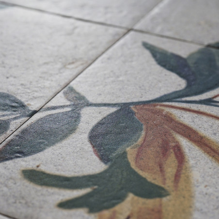 Eine Fliese mit Blumenmuster zeigt grüne und braune Blätter, was auf eine künstlerische Dekoration schließen lässt. Das Motiv er