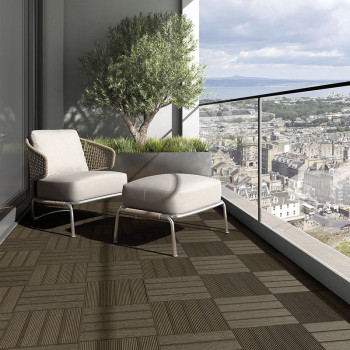 A wicker chair and ottoman set rest on a geometric-patterned balcony, overlooking a sprawling cityscape with distant mountains.