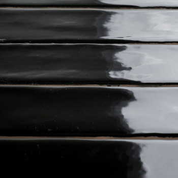 Shiny black ceramic tiles reflect light, creating a glossy surface. The tiles are arranged in parallel rows, suggesting an inter