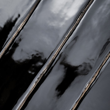 Sleek, glossy black tiles reflect light, creating wavy distortions and capturing abstract reflections in a smooth, minimalist se