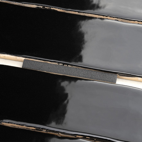 Black glossy ceramic tiles lie parallel with thin, beige grout lines separating them, reflecting a soft light pattern across the