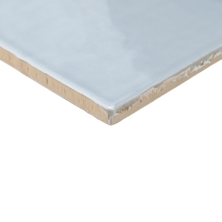Un carreau de céramique bleu clair brillant avec une surface lisse repose en angle, mettant en valeur son bord beige inachevé su
