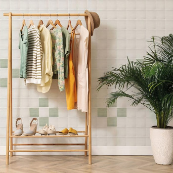 Op een houten kledingrek hangen zes hangende outfits, met daaronder hoeden en schoenen. Hij staat tegen een betegelde muur naast