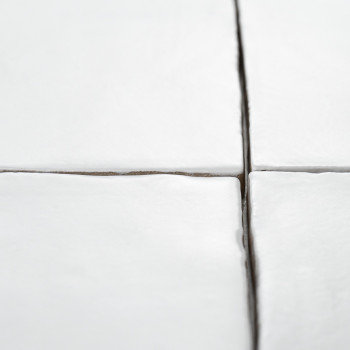 Os ladrilhos cerâmicos brancos formam uma grade com linhas de argamassa visíveis em um espaço limpo e minimalista. Bordas ligeir