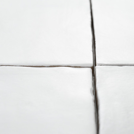 Los azulejos cerámicos blancas forman una cuadrícula con líneas de lechada visibles en un espacio limpio y minimalista. Bordes l