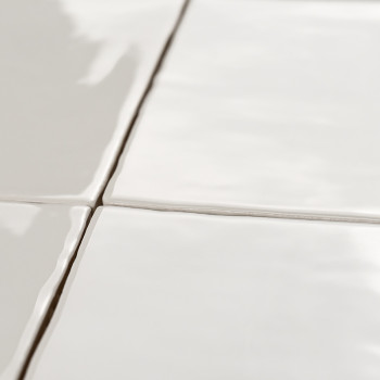 Cuatro azulejos de cerámica blanca brillante forman una cuadrícula, unidas por finas líneas de lechada, que reflejan la luz en u
