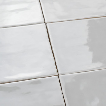 Les carreaux blancs lisses et brillants sont soigneusement disposés selon un motif en grille, reflétant la lumière dans une pièc