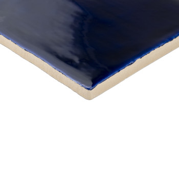 Un azulejo cerámico brillante de color azul intenso refleja la luz y muestra su suave superficie vidriada contra un borde beige 