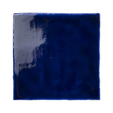Un azulejo cuadrado, brillante y de color azul intenso refleja la luz, resaltando su textura suave y su acabado monocromático, s