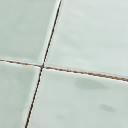 Cuatro azulejos de cerámica de color verde pálido brillante se cruzan, formando una cuadrícula desigual con líneas de lechada vi