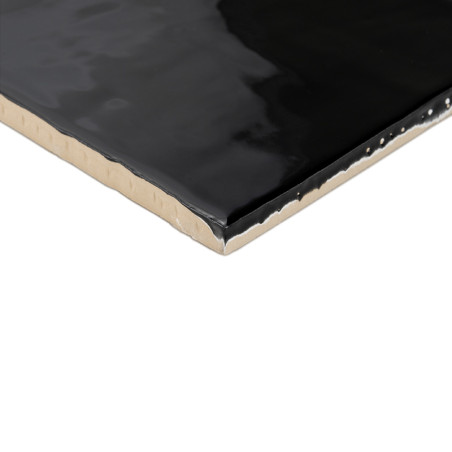 Eine glänzende schwarze Keramikfliese mit leicht rauer Kante liegt vor einem weißen Hintergrund und reflektiert das Licht dezent Eine glänzende schwarze Keramikfliese mit leicht rauer Kante liegt vor einem weißen Hintergrund und reflektiert das Licht dezent