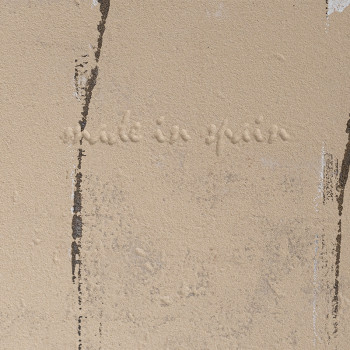 Un azulejo beige muestra el texto grabado `made in spain`, con rayas verticales irregulares de color marrón que se asemejan a pa