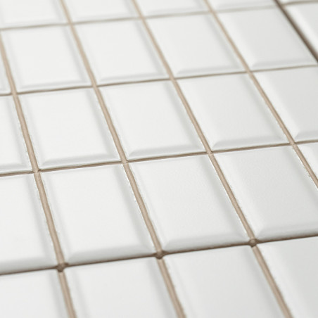 Les carreaux de céramique blanche sont soigneusement disposés selon un motif en grille, légèrement surélevés en leur centre, cré