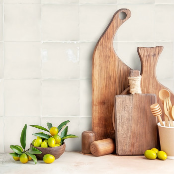 Tábuas de corte de madeira ficam em pé contra a parede de azulejos da cozinha, acompanhadas por uma tigela de azeitonas verdes e