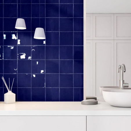Los azulejos cuadrados azules adornan una pared y reflejan la luz sutilmente. Cerca de allí, una moderna configuración de lavabo