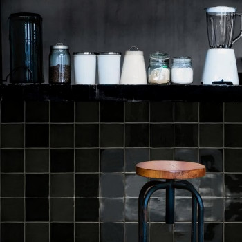 En la encimera de la cocina hay una licuadora, frascos y un recipiente. Debajo, un taburete de madera se alza contra las paredes