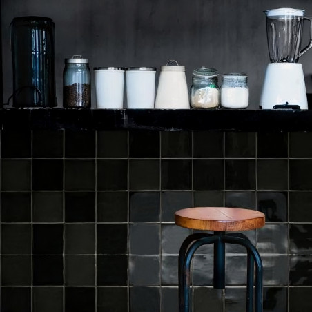 Auf einer Küchentheke stehen ein Mixer, Gläser und ein Kanister. Unten steht ein Holzhocker vor dunkel gefliesten Wänden. Auf einer Küchentheke stehen ein Mixer, Gläser und ein Kanister. Unten steht ein Holzhocker vor dunkel gefliesten Wänden.