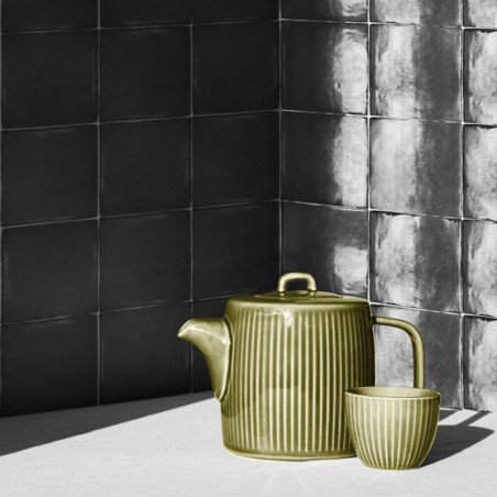 Een groene, geribbelde theepot en bijpassende kop staan ​​in het zonlicht tegen een achtergrond van donkere, gestructureerde vie