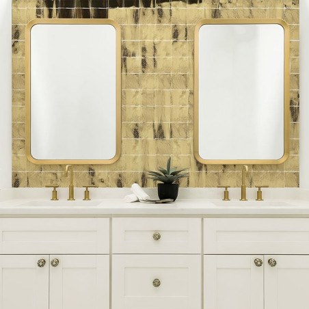 Deux miroirs rectangulaires avec des cadres dorés se reflètent sur un mur texturé carrelé d'or. Ci-dessous, des lavabos doubles 
