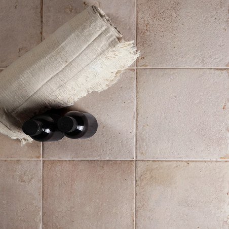 Uma toalha de linho enrolada e duas garrafas pretas repousam sobre uma grade de azulejos quadrados bege e levemente texturizados Uma toalha de linho enrolada e duas garrafas pretas repousam sobre uma grade de azulejos quadrados bege e levemente texturizados