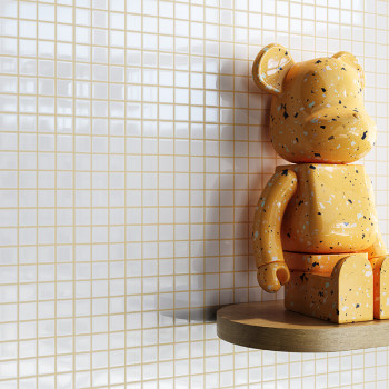 Auf einem Holzregal sitzt eine orangefarbene, gesprenkelte Bärenfigur. Es steht vor einem Hintergrund aus kleinen, weißen, quadr