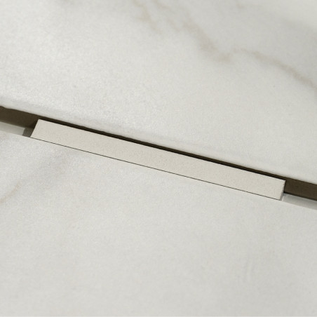Un carreau rectangulaire beige clair repose légèrement en hauteur sur un fond assorti, révélant un étroit espace sombre en desso