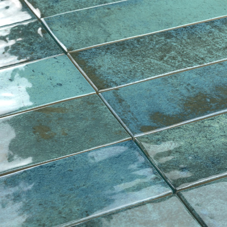 Ladrilhos retangulares brilhantes em tons de azul e verde ficam lado a lado, refletindo a luz em uma superfície texturizada.