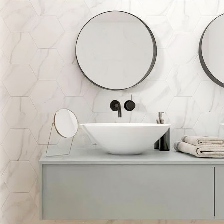 A round mirror hangs on a bathroom wall, above a modern white sink. The setting includes minimalistic decor and hexagonal wall t