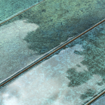 Os revestimentos cerâmicos retangulares apresentam acabamento brilhante e manchado com tons de verde e azul, dispostos em um pad