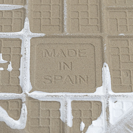 A textured tile displays the stamped text `MADE IN SPAIN,` surrounded by grout lines and partially covered in white grout, sugge