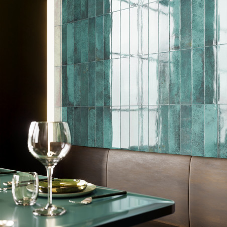 Des carreaux rectangulaires bleu sarcelle recouvrent un mur, réfléchissant la lumière dans une salle à manger. Un verre et des c