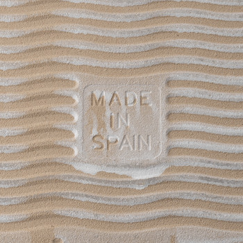 Sand-textured tile with `MADE IN SPAIN` embossed. wavy patterns create a rippled effect, suggesting a beach-like environment.
