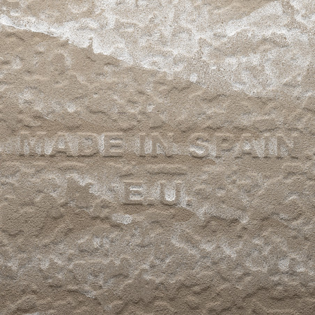 Un carreau beige texturé présente un texte en relief indiquant « MADE IN SPAIN E.U. » sur une surface inégale semblable à de la 