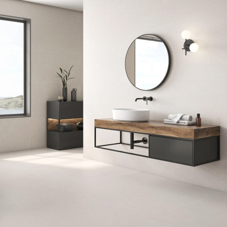 A round mirror hangs above a modern sink on a wooden vanity in a minimalist bathroom with beige walls, near a large window. A round mirror hangs above a modern sink on a wooden vanity in a minimalist bathroom with beige walls, near a large window.