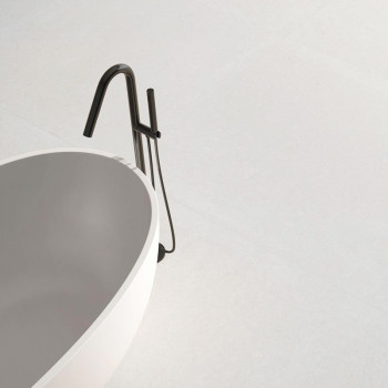 A sleek white bathtub sits on a smooth, expansive light gray floor, accompanied by a modern black faucet, creating a minimalist 