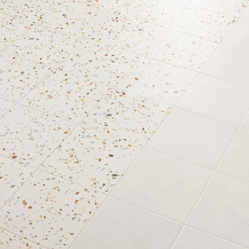 Les carreaux passent du terrazzo, tacheté d'éclats multicolores, au blanc uni, créant un motif sur la surface lisse du sol.